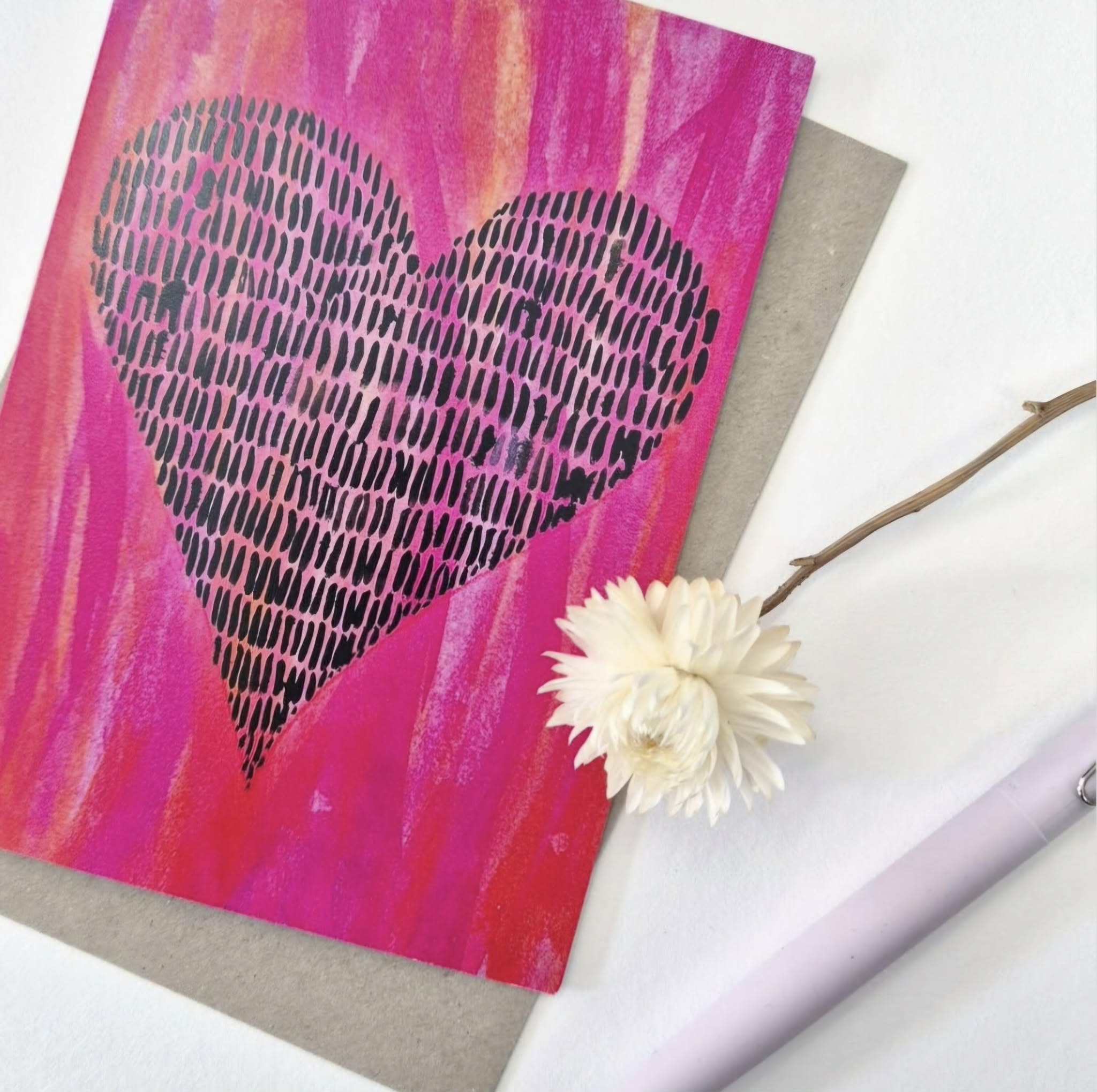 A greeting card that has a magenta coloured watercolour background with a heart shape formed by lots of little black ink vertical strokes.